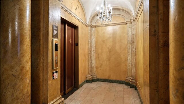 corridor with a notable chandelier, light tile patterned flooring, lofted ceiling, and ornamental molding