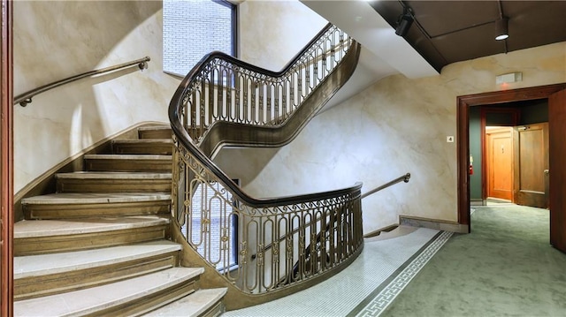 staircase featuring carpet flooring, rail lighting, and a towering ceiling