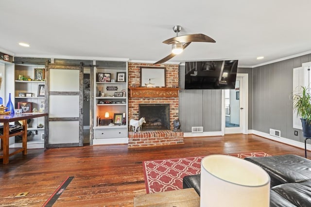 living room featuring crown molding, hardwood / wood-style flooring, ceiling fan, a brick fireplace, and a barn door