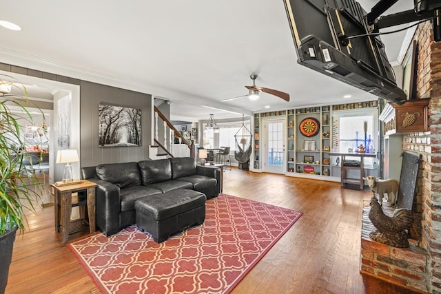 living room with hardwood / wood-style floors, ceiling fan with notable chandelier, ornamental molding, and a brick fireplace