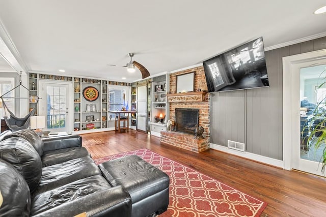 living room with crown molding, a fireplace, built in features, and wood-type flooring