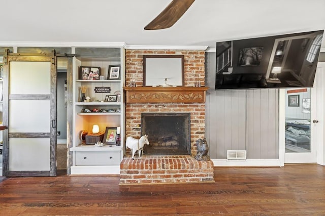 living room with a fireplace, dark wood-type flooring, ornamental molding, and a barn door