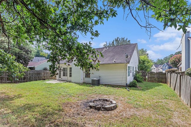 back of property with an outdoor fire pit, central AC unit, and a lawn