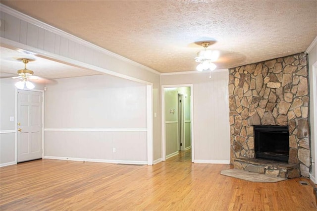 unfurnished living room featuring a ceiling fan, a stone fireplace, a textured ceiling, and wood finished floors