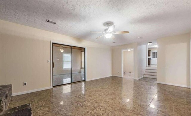 empty room featuring a textured ceiling, visible vents, baseboards, and ceiling fan