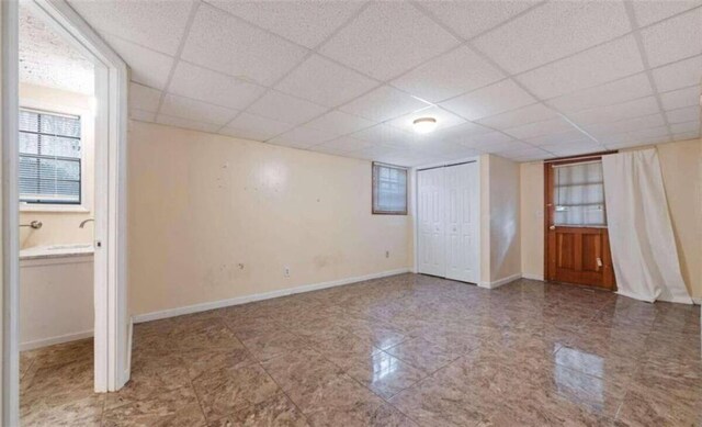 below grade area with baseboards, a drop ceiling, and tile patterned floors