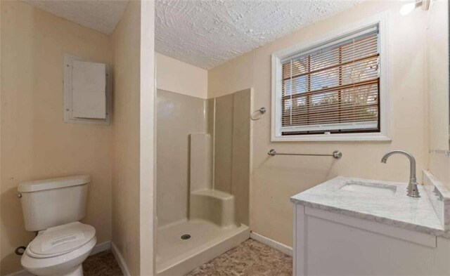 bathroom with a stall shower, a textured ceiling, baseboards, toilet, and vanity