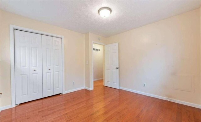 unfurnished bedroom featuring a textured ceiling, baseboards, visible vents, and light wood-style floors