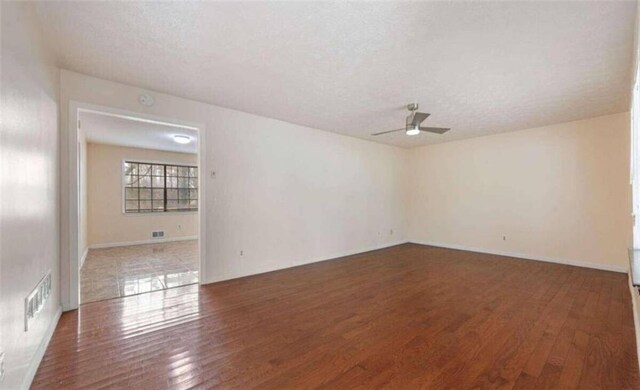 empty room featuring a textured ceiling, visible vents, wood finished floors, and a ceiling fan