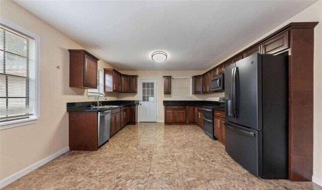 kitchen with a sink, dark countertops, dark brown cabinetry, baseboards, and appliances with stainless steel finishes