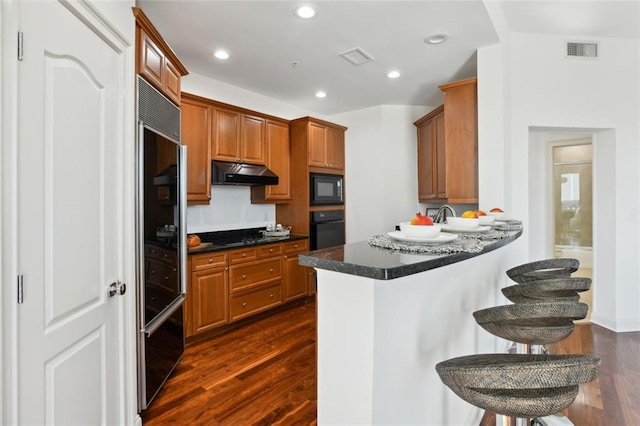 2828 Peachtree Rd NW Unit 1502, Atlanta, GA 30305 - kitchen with black appliances, under cabinet range hood, dark wood-type flooring, a kitchen breakfast bar, and a peninsula