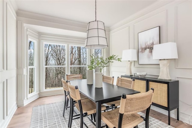 dining area with ornamental molding, light wood-style flooring, and a decorative wall