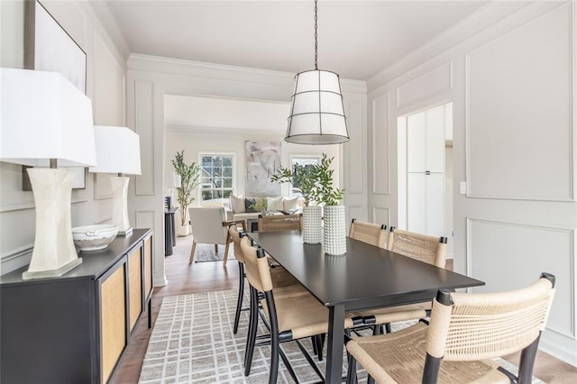 dining area with crown molding, light wood-type flooring, and a decorative wall