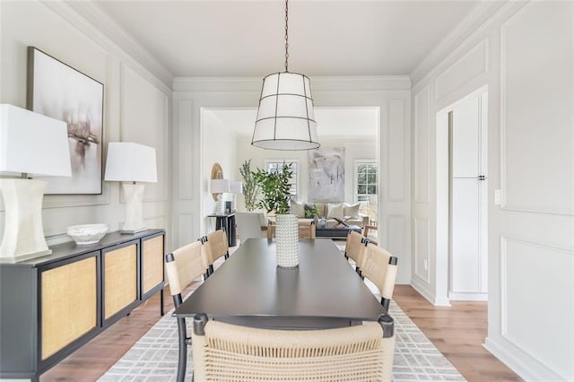 dining room featuring crown molding, light wood-type flooring, and a decorative wall