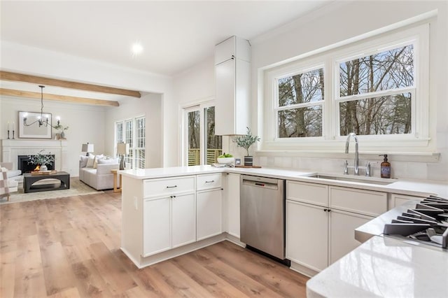 kitchen featuring a warm lit fireplace, light wood finished floors, a peninsula, stainless steel dishwasher, and a sink