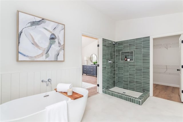 full bathroom featuring a freestanding bath, a spacious closet, tiled shower, and wainscoting