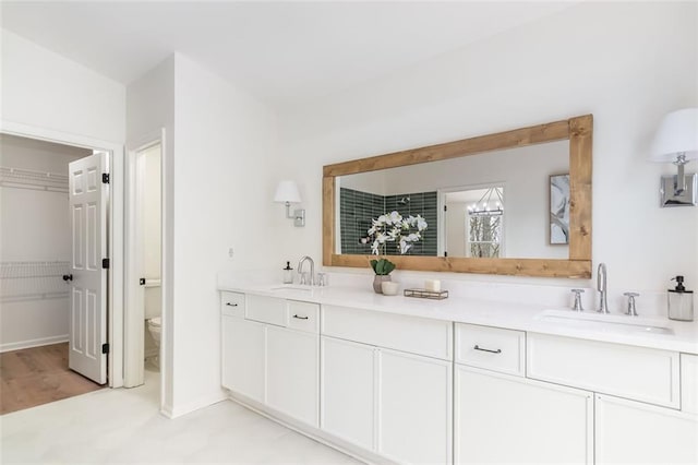 full bath with toilet, double vanity, baseboards, and a sink