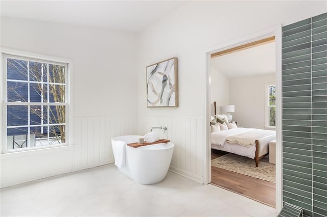 ensuite bathroom with wood finished floors, a soaking tub, wainscoting, and connected bathroom