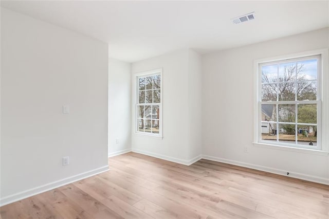 unfurnished room with light wood-type flooring, baseboards, visible vents, and a wealth of natural light