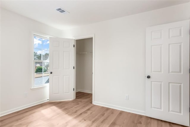 unfurnished bedroom featuring light wood-type flooring, baseboards, a spacious closet, and visible vents