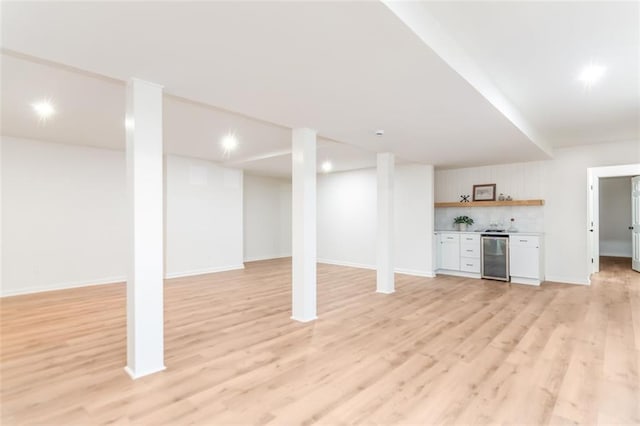 finished below grade area featuring wine cooler, baseboards, light wood-style flooring, and a dry bar