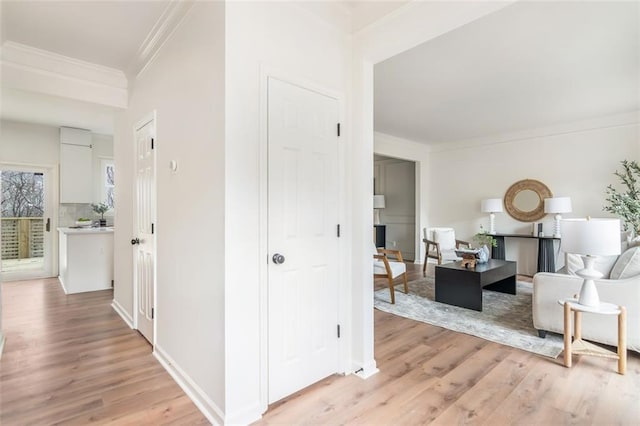 corridor featuring light wood-style floors, ornamental molding, and baseboards