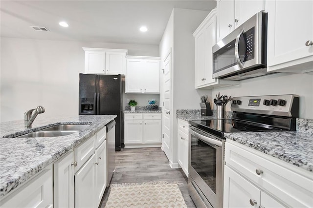 kitchen with stainless steel appliances, a sink, light wood finished floors, white cabinets, and recessed lighting