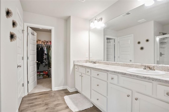 full bath with a stall shower, wood finished floors, double vanity, a spacious closet, and baseboards