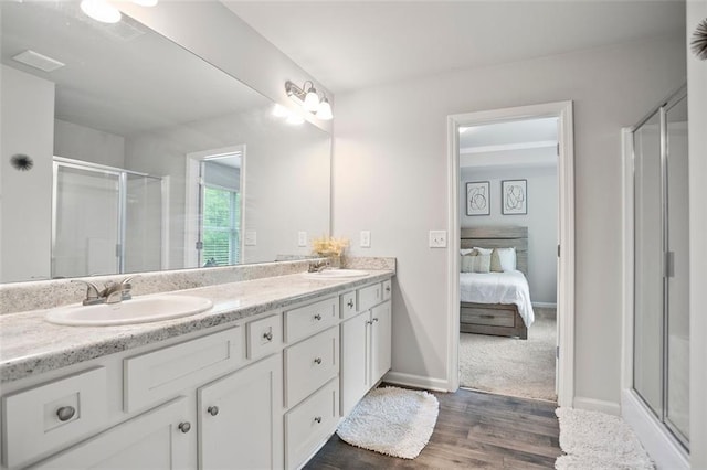full bathroom with a shower stall, wood finished floors, double vanity, and ensuite bathroom
