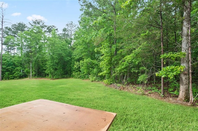 view of green lawn with a patio area and a forest view