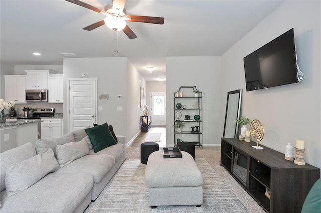 living room featuring ceiling fan, light carpet, and baseboards