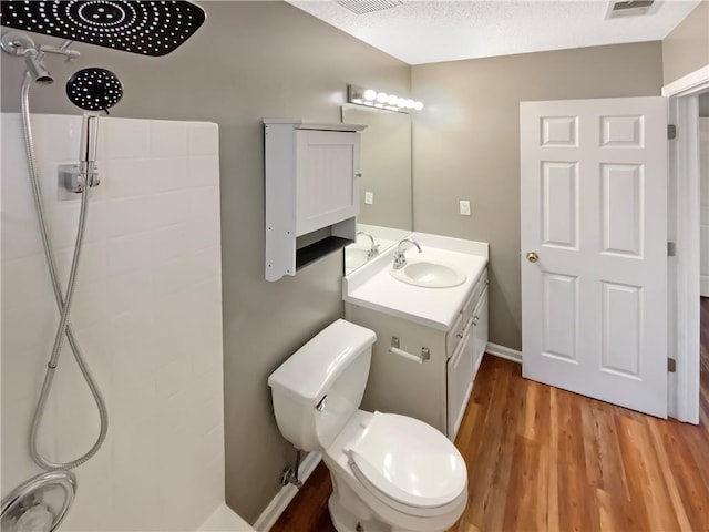 bathroom featuring toilet, vanity, a tile shower, wood finished floors, and a textured ceiling