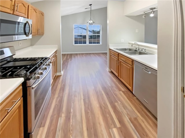 kitchen with light wood finished floors, light countertops, lofted ceiling, appliances with stainless steel finishes, and a sink