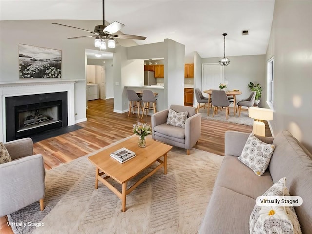 living room featuring a fireplace with flush hearth, a ceiling fan, baseboards, light wood-style floors, and lofted ceiling