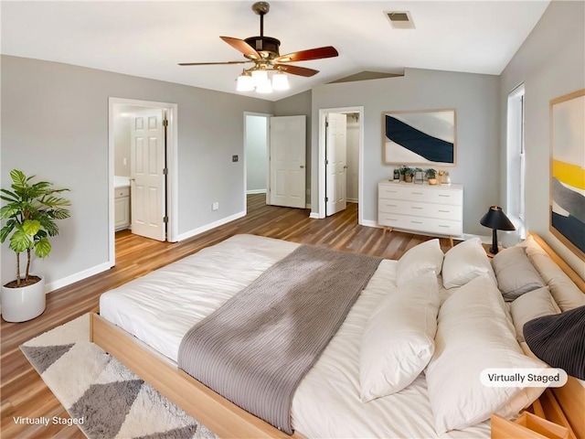 bedroom with visible vents, a walk in closet, baseboards, vaulted ceiling, and wood finished floors