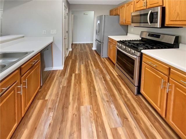 kitchen with baseboards, a sink, stainless steel appliances, light countertops, and light wood-type flooring