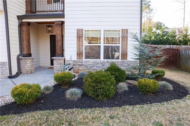 property entrance with a balcony, stone siding, and fence