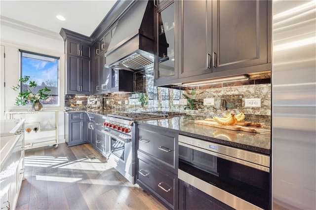 661 Auburn Ave NE Unit 10, Atlanta, GA 30312 - kitchen featuring premium appliances, custom exhaust hood, light wood finished floors, dark stone countertops, and decorative backsplash