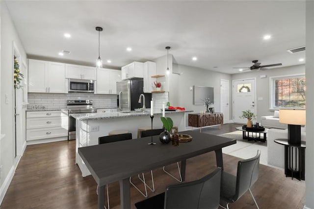 kitchen featuring white cabinetry, ceiling fan, decorative light fixtures, a center island with sink, and appliances with stainless steel finishes