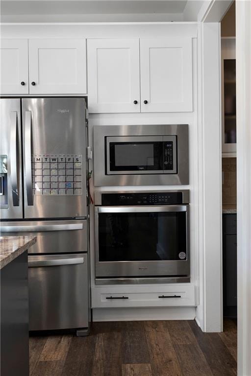 kitchen featuring white cabinets, appliances with stainless steel finishes, dark hardwood / wood-style flooring, and light stone countertops