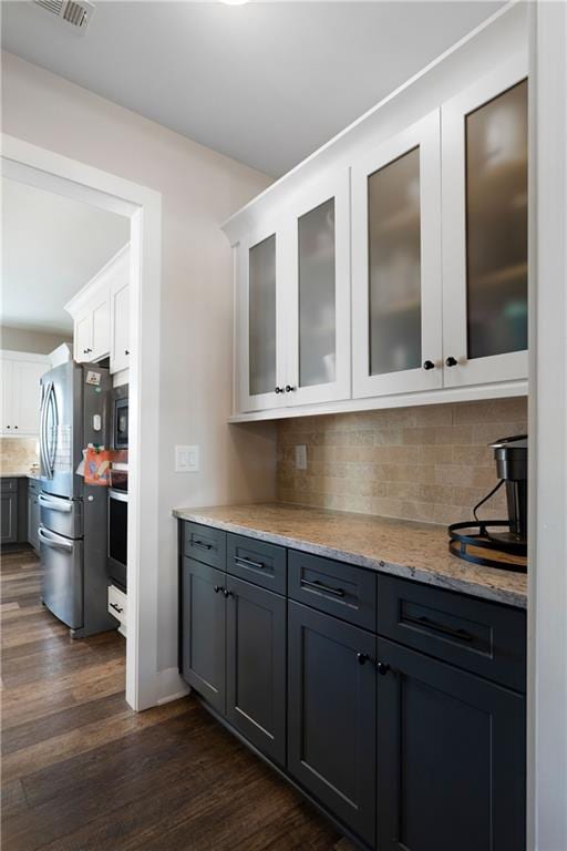 bar with white cabinetry, decorative backsplash, stainless steel refrigerator, dark hardwood / wood-style floors, and light stone counters