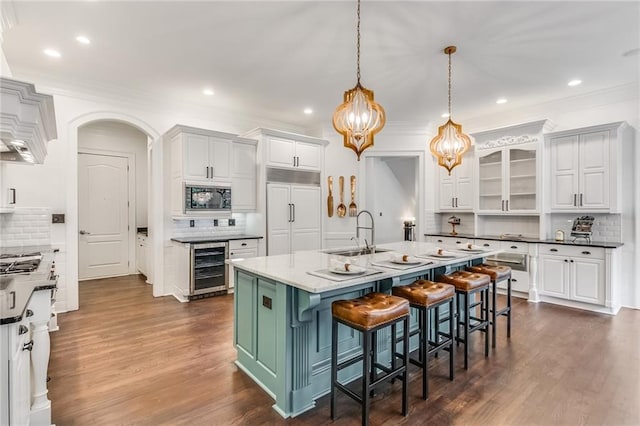 kitchen with sink, white cabinetry, built in appliances, wine cooler, and a center island with sink