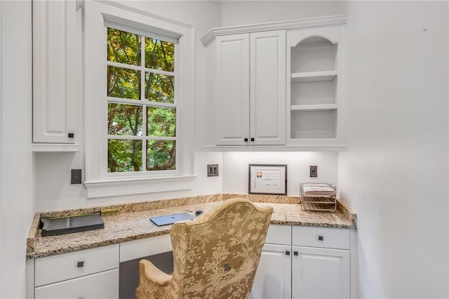 bar with built in desk, light stone counters, and white cabinetry