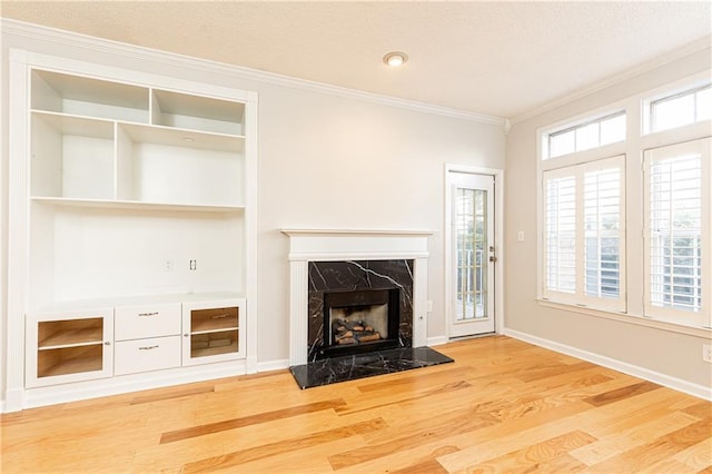 unfurnished living room featuring built in shelves, a fireplace, wood finished floors, baseboards, and crown molding