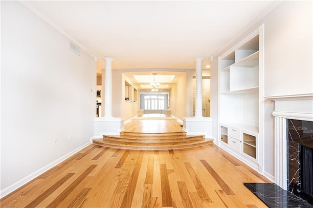 corridor with crown molding, ornate columns, light wood-style flooring, an inviting chandelier, and baseboards