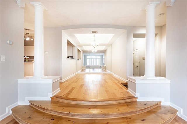 hall featuring wood finished floors, decorative columns, and baseboards