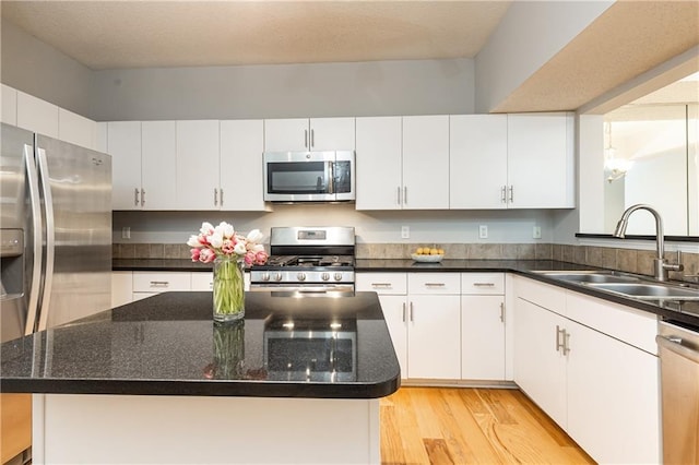 kitchen with light wood finished floors, white cabinets, a center island, stainless steel appliances, and a sink