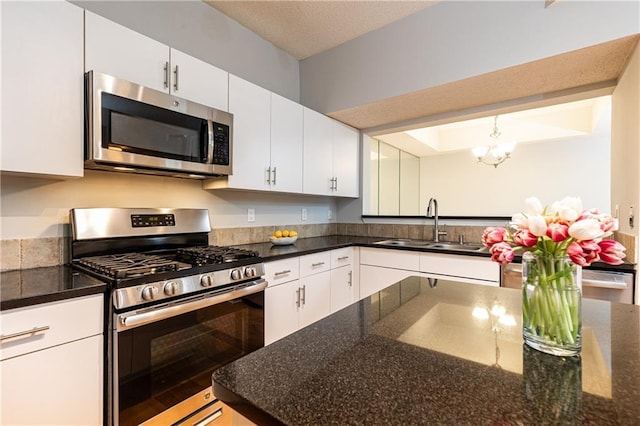 kitchen featuring an inviting chandelier, appliances with stainless steel finishes, white cabinetry, a sink, and dark stone countertops