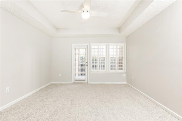 spare room with a ceiling fan, a tray ceiling, carpet flooring, and baseboards