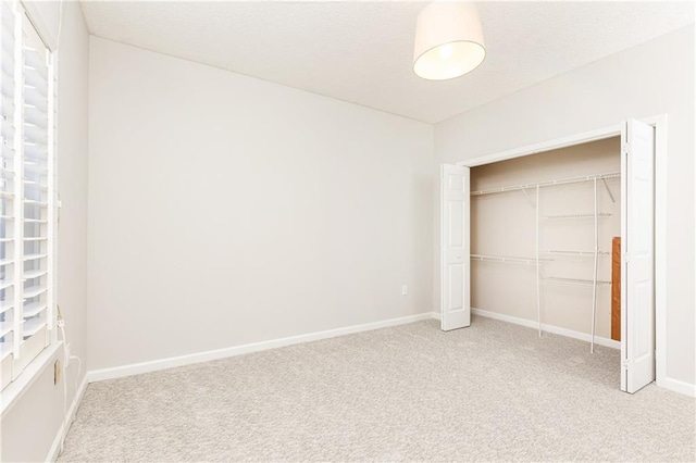 unfurnished bedroom with baseboards, a closet, and light colored carpet